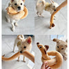 A fluffy dog is playing with an orange squeaky plush toy shaped like a dachshund.