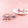 Pink lace bow cat collar with a bell and bead charm displayed on a white plate.