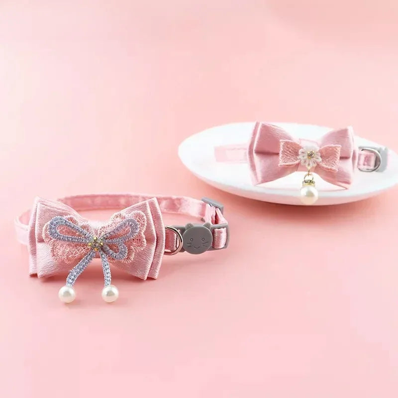 Pink lace bow cat collar with a bell and bead charm displayed on a white plate.