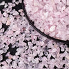 Pink rose quartz crystal chips scattered on a dark surface.
