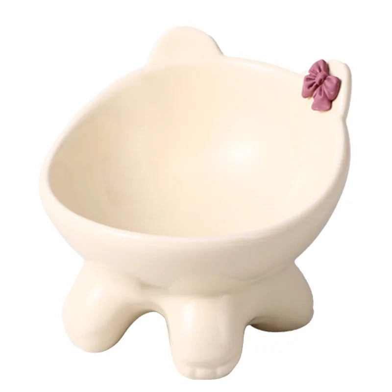 A cream-colored ceramic cat food bowl with a raised, tilted design and a pink bow decoration.