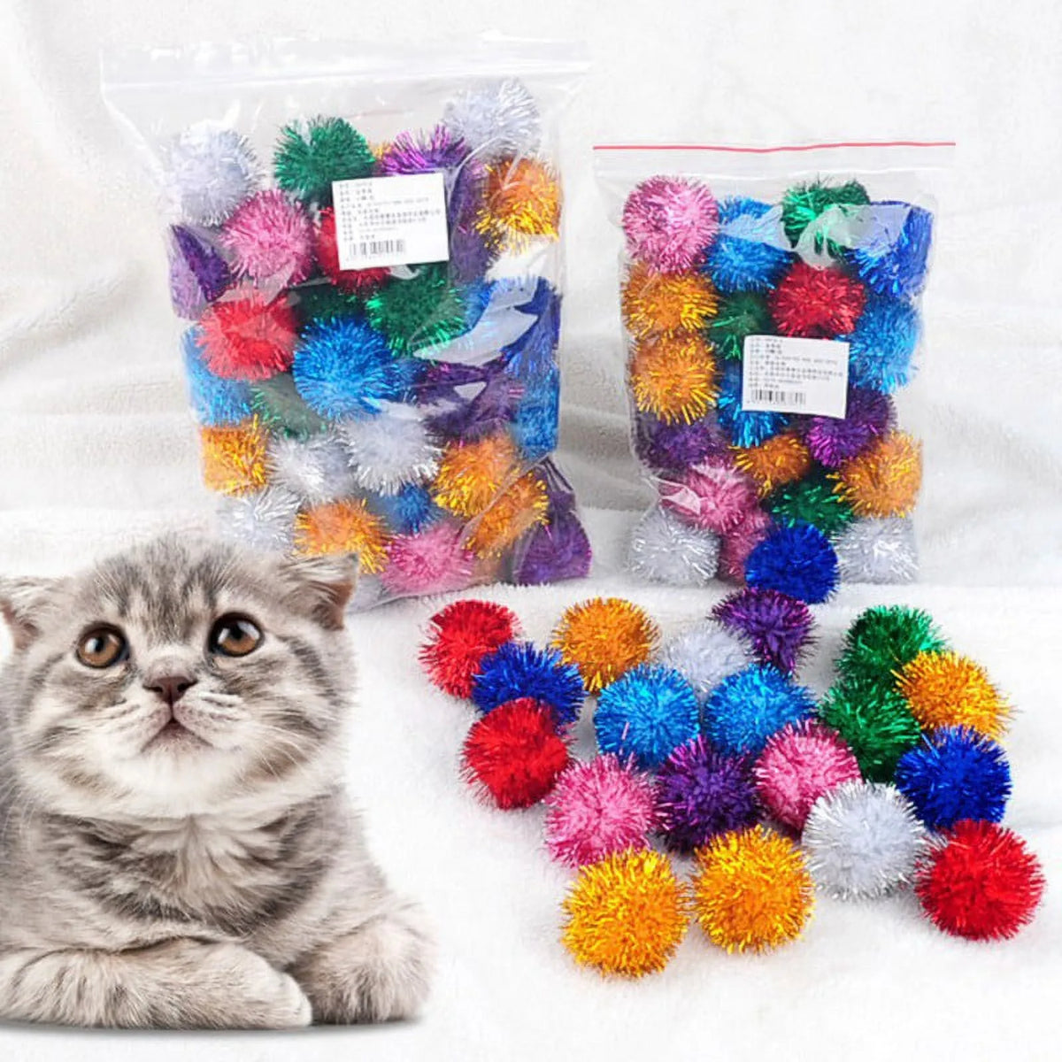 Two bags of colorful crinkle pet balls for cats and kittens with a kitten sitting in the foreground