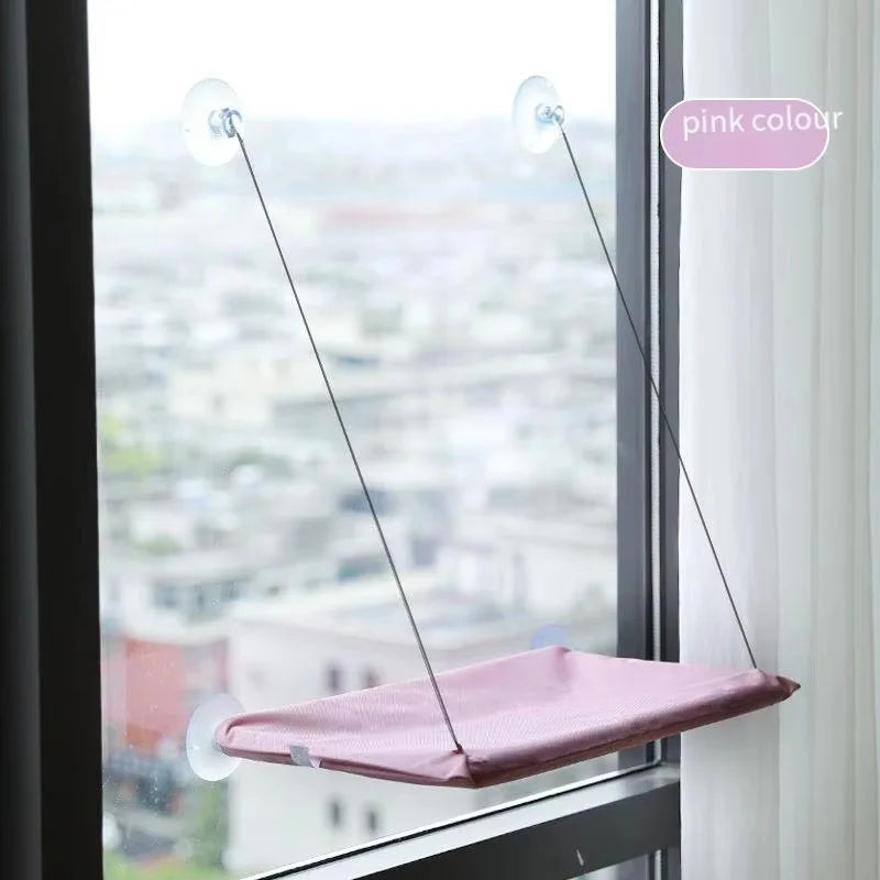 Lit-hamac avec ventouse rose suspendu dans une fenêtre avec vue sur un paysage urbain.