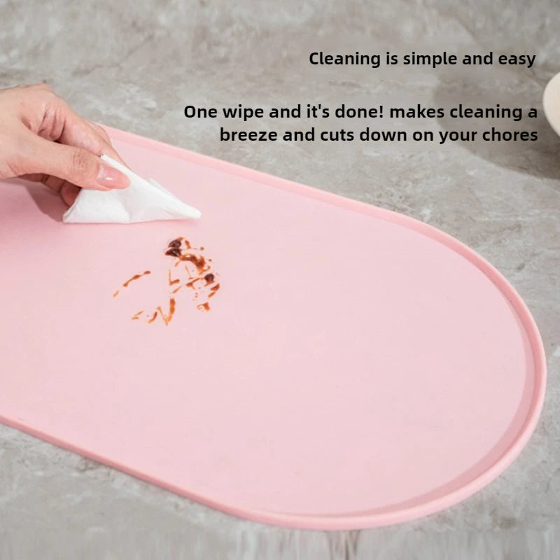 A pink non-slip feeding mat is being wiped clean with a white cloth, demonstrating easy cleaning.
