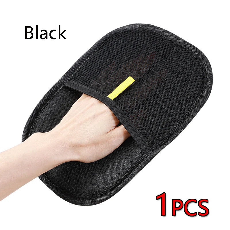 A hand is holding a black pet grooming glove with a yellow tab, showing the product for hair removal and cleaning.