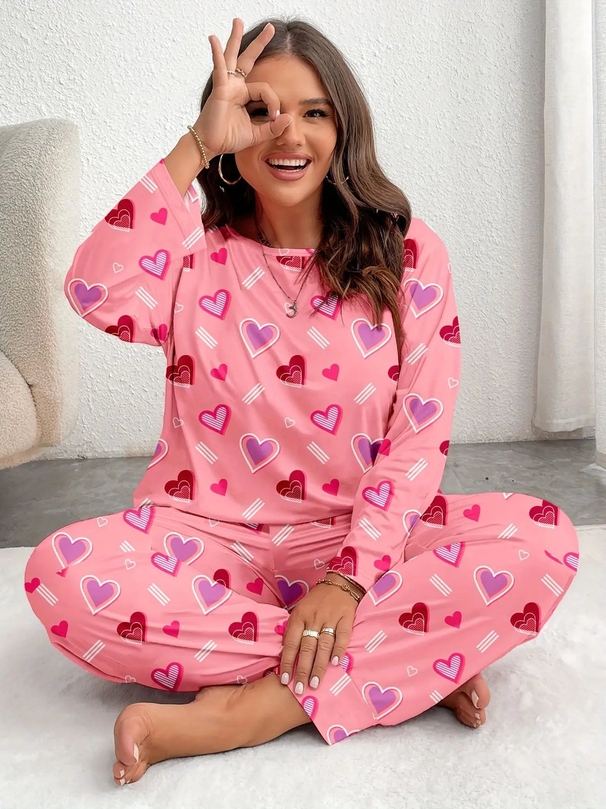A woman models a pink heart print pajama set while making a peace sign.