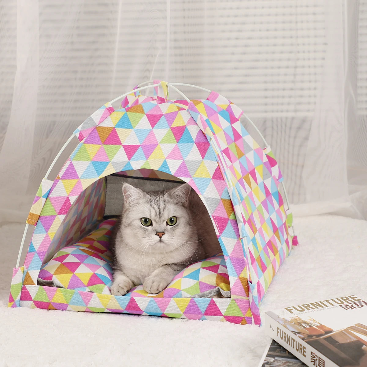 Lit de voyage pour chat à motifs géométriques roses et colorés sur une surface blanche.