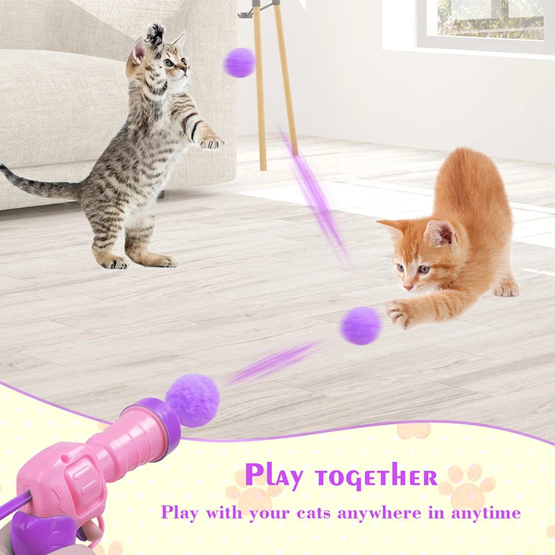 A pink plush ball launcher is shown with purple balls being launched toward a kitten.