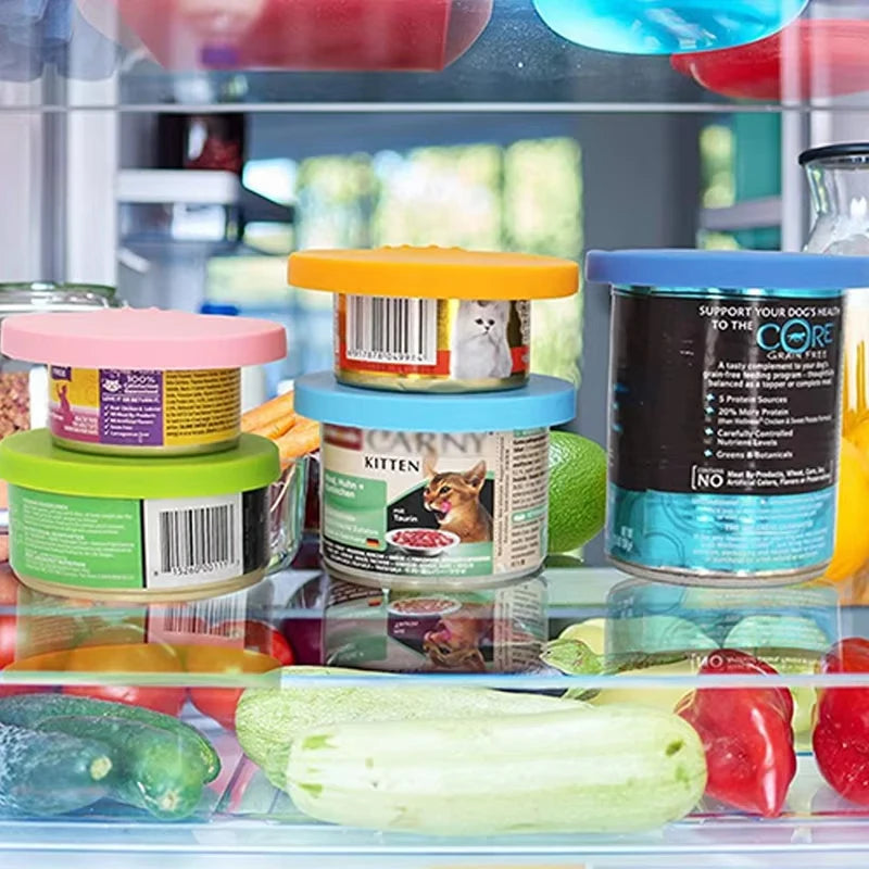A collection of reusable silicone pet food can lids and spoons in various colors displayed in a glass container.