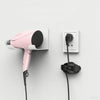 A pink hair dryer is mounted on a wall, with its cord hanging down. A silicone cable organizer is visible below.