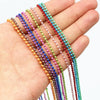 A hand holds a set of ball necklaces featuring various colors including gold, silver, pink, purple, green, and red.