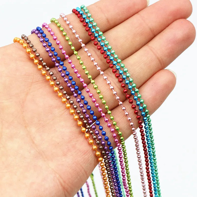 A hand holds a set of ball necklaces featuring various colors including gold, silver, pink, purple, green, and red.