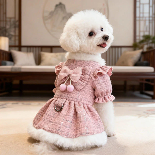 A fluffy white dog wearing a pink tweed dress with a bow and pom-pom trim sitting on a light rug.