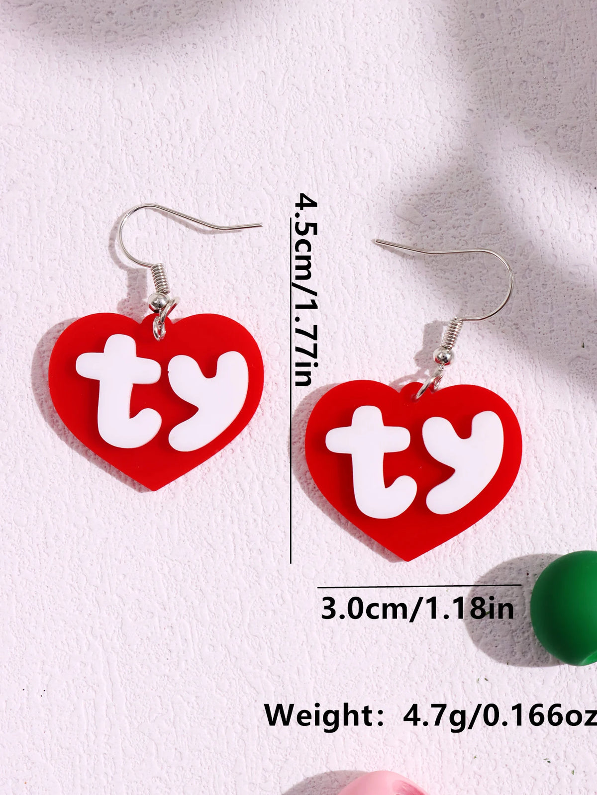 Red acrylic heart stud earrings with a white initial design and silver ear hooks