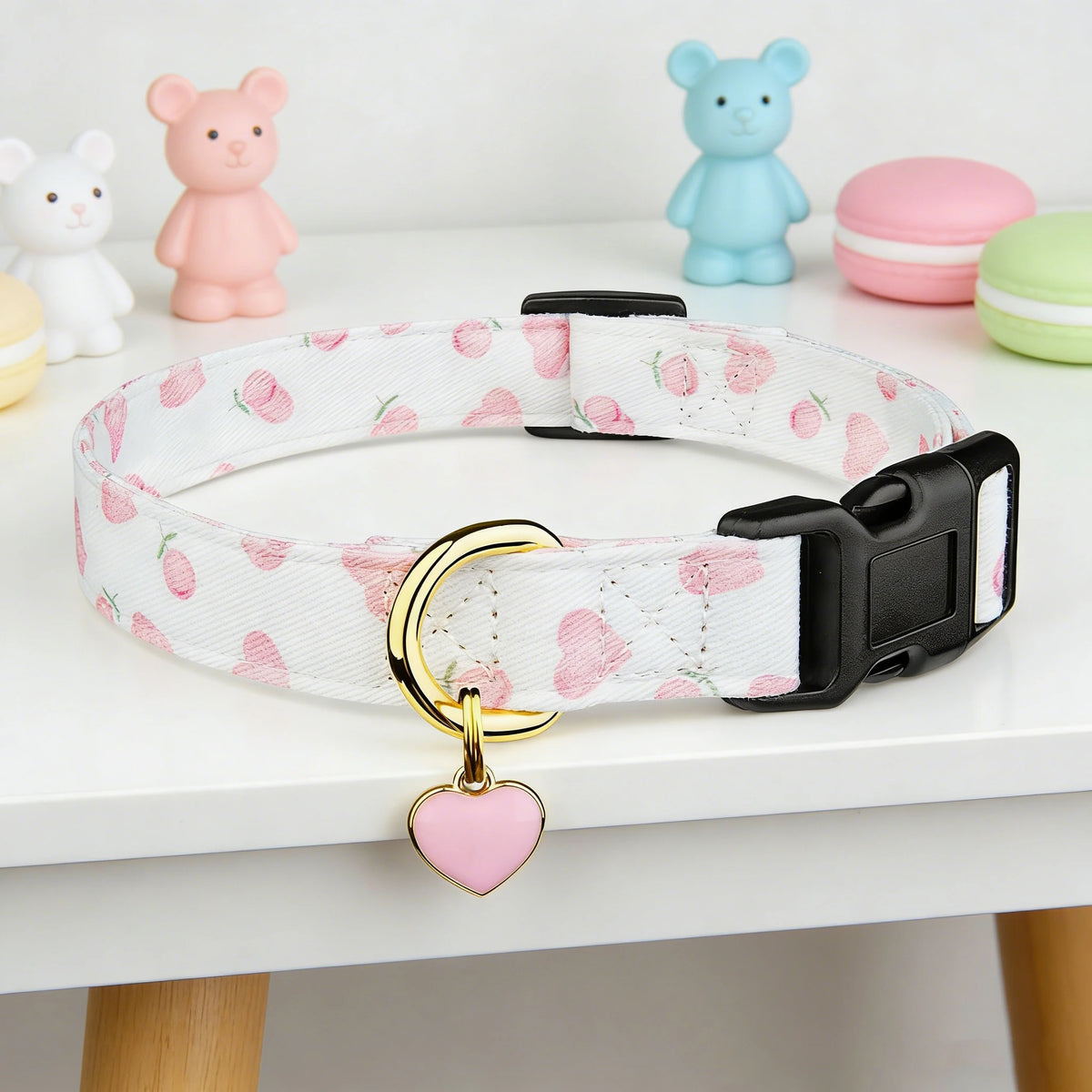 Weißer Baumwollhalsband für Hund mit rosa Erdbeere-Anhänger und schwarzer Schnalle, auf weißem Tisch.