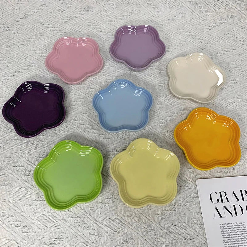 A collection of colorful ceramic flower-shaped pet bowls and dipping dishes in shades of pink, purple, blue, cream, and yello