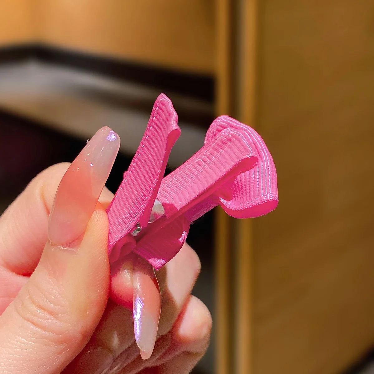 A hand holds a pink fabric hair clip set with pink and white accents against a blurred background.