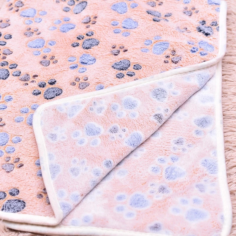 A pink flannel fleece pet blanket featuring a blue paw print pattern.