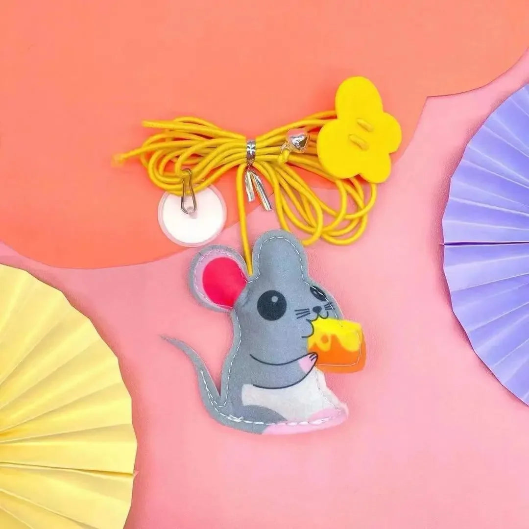 A gray cat toy with pink accents is hanging from a yellow rope against a pink background.
