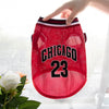A red basketball vest for a dog with the number 23 is being held by a hand.