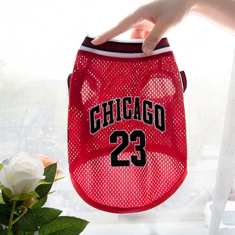 A red basketball vest for a dog with the number 23 is being held by a hand.