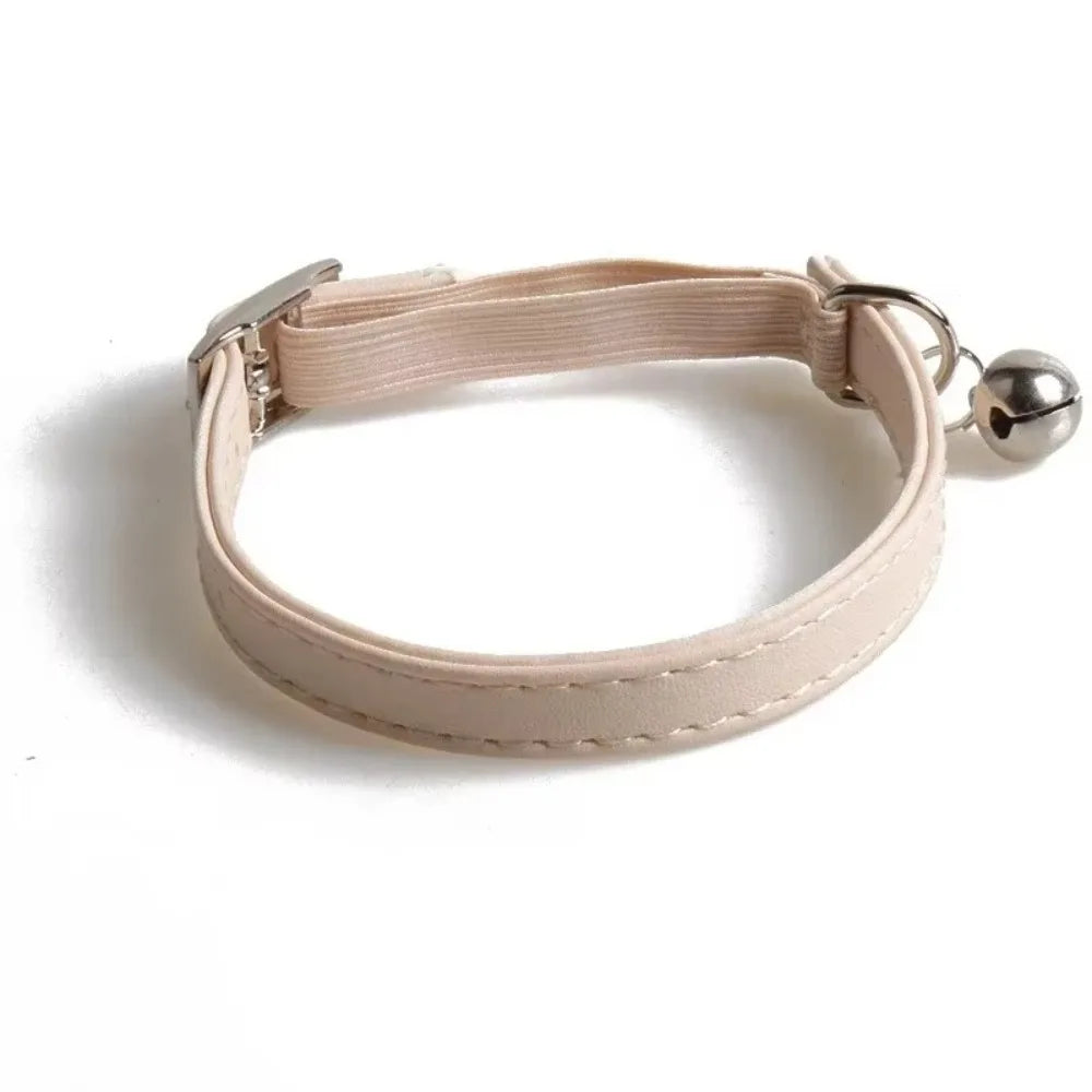 A light beige adjustable cat collar made of soft PU leather with an elastic webbing strap and a small metal bell.