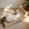 Un gato blanco y negro está relajándose en un rascador vertical de sisal natural en interiores.