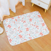 A white mat featuring a floral pattern of red and light blue flowers and small gray animal figures on a wooden floor.
