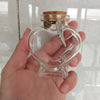 A clear glass heart-shaped jar with a cork stopper and a feather decoration is held in a hand.