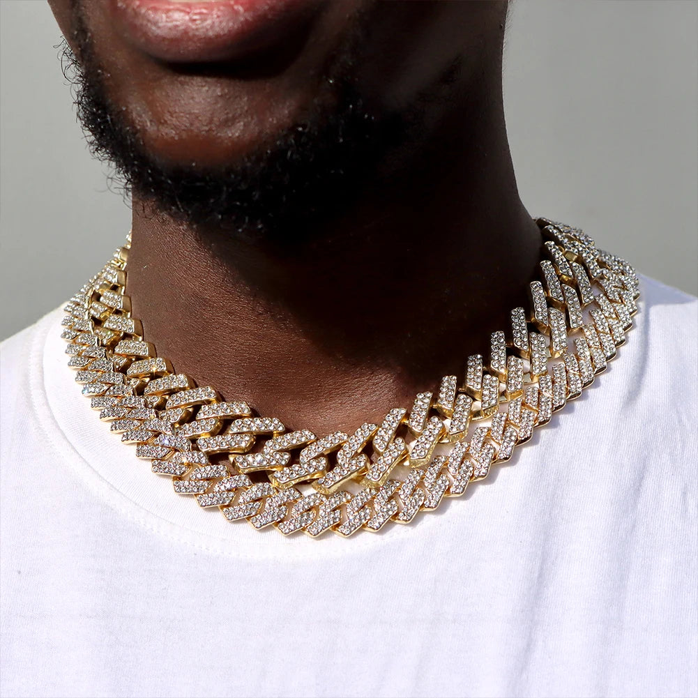 A close-up of a gold iced out Cuban link chain necklace with rhombus diamond accents worn around a man's neck.