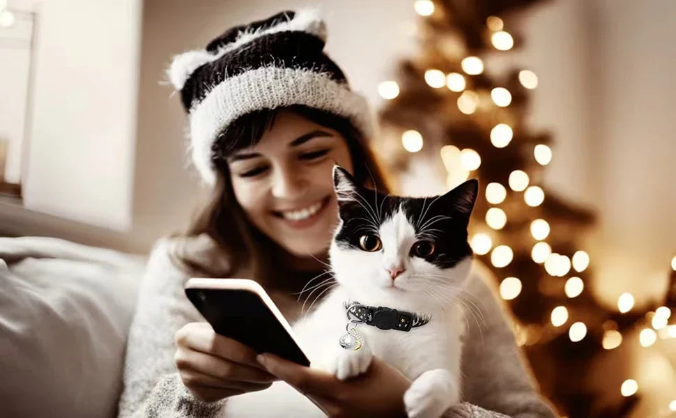 A woman is smiling while holding a smartphone, petting a black and white cat in a cozy indoor setting with a blurred Christma