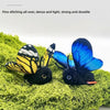 A black felted cat toy with blue and yellow butterfly wings is resting on green moss.