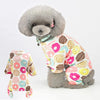 A fluffy gray dog wearing a patterned cotton pajama top with various colorful designs.