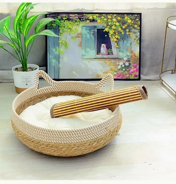 A woven rattan cat bed with a removable cushion sits on a light wooden floor in front of a framed nature print.