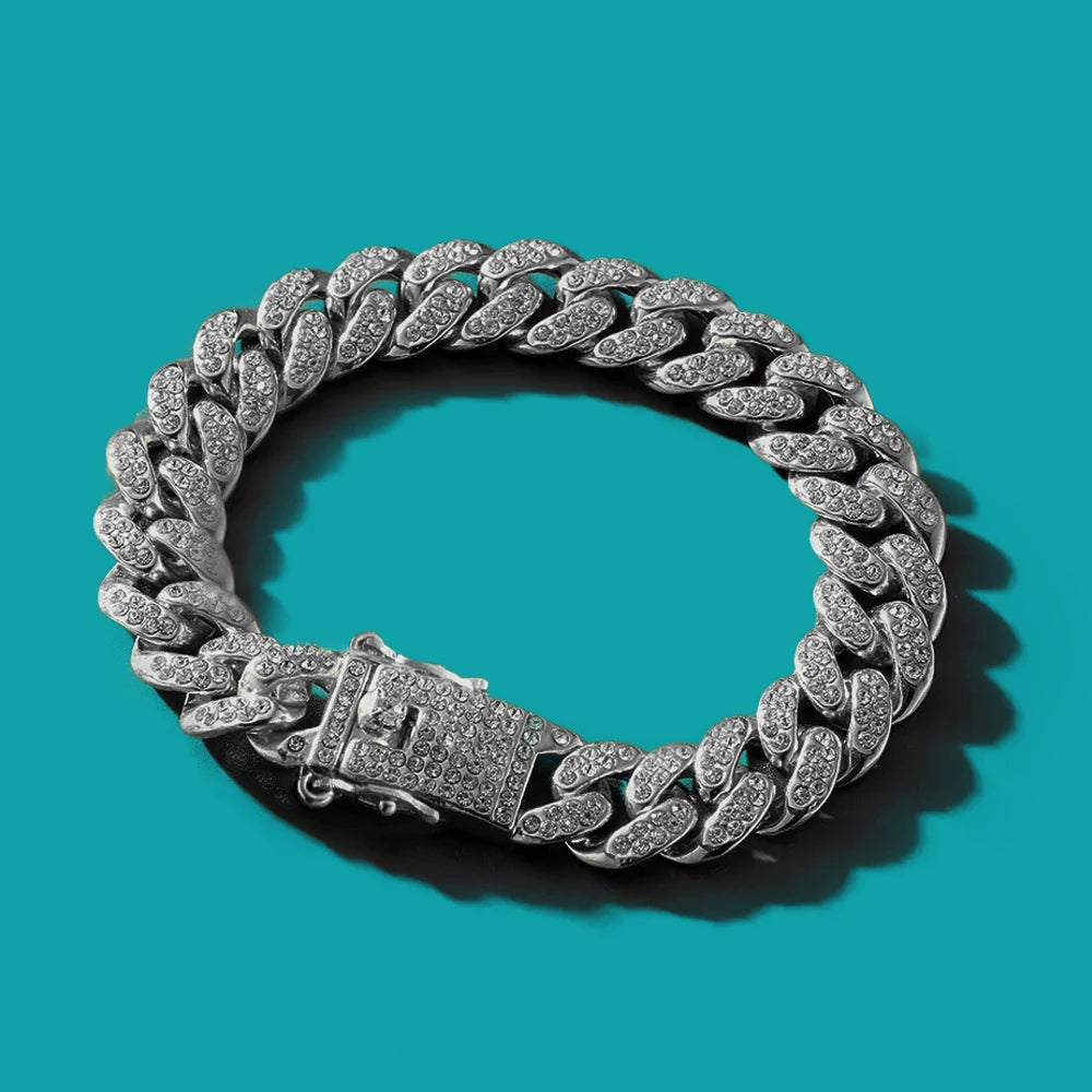 Un collier à maillons cubains argentés est exposé sur un fond bleu sarcelle.