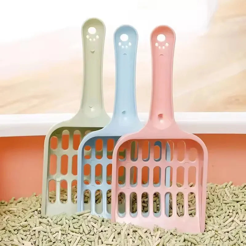 A set of five plastic cat litter scoops in pastel colors, including mint green, light blue, and pink, resting on a bed of lig