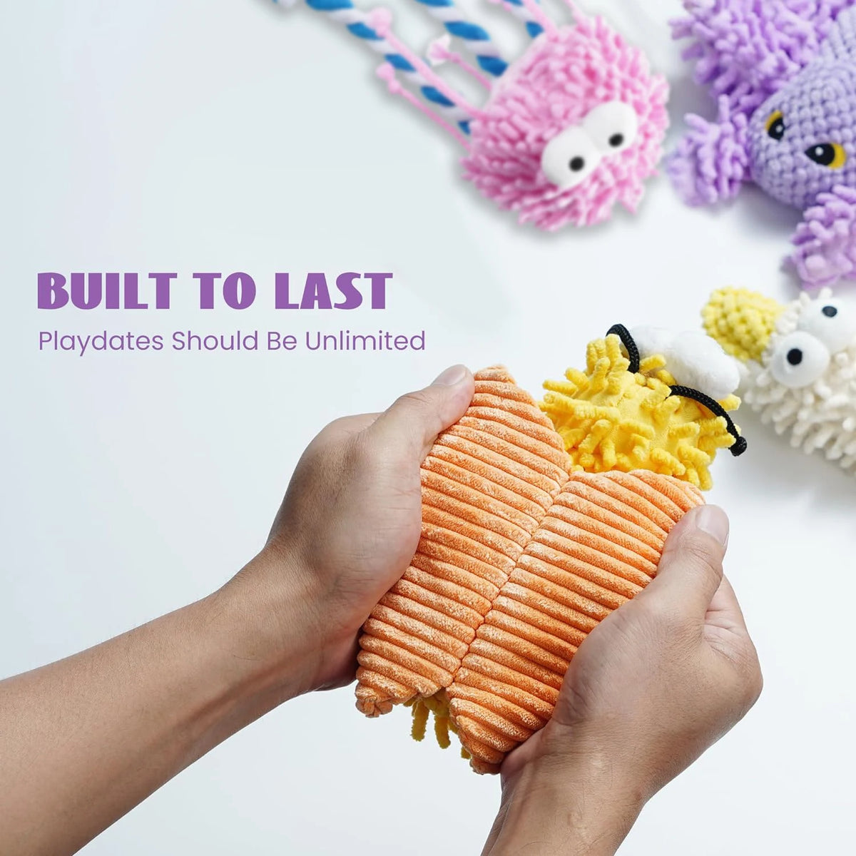 A hand is holding an orange crinkly plush toy dog toy with a black nose, surrounded by other colorful squeaky toys.