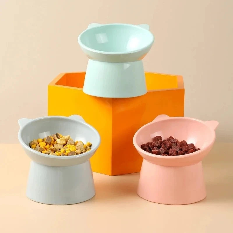A set of three pet feeding bowls in white, light green, and pink, displayed on a wooden surface.