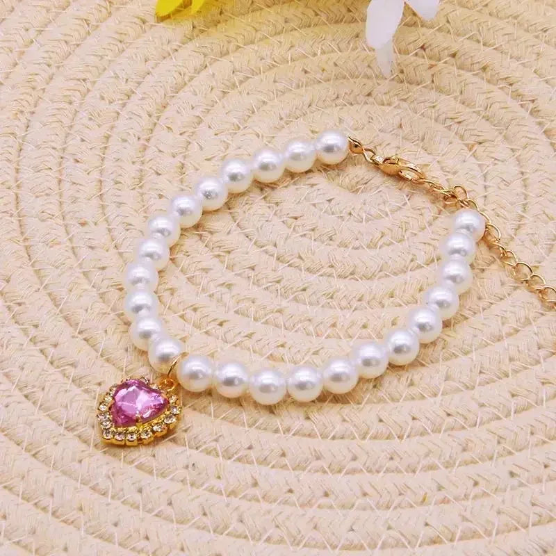 A pearl necklace with a pink gemstone pendant is displayed on a light beige textured background.