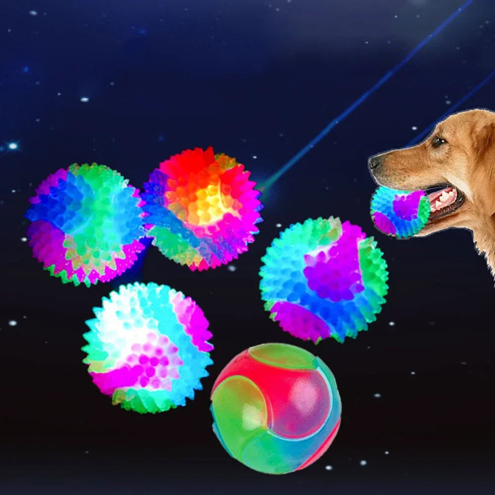 A golden dog is playfully interacting with several brightly colored glowing rubber fetch balls against a dark, starry backgro