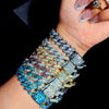A close-up of a hand wearing an iced-out Cuban link bracelet featuring multicolored rhinestones and pavé stones.
