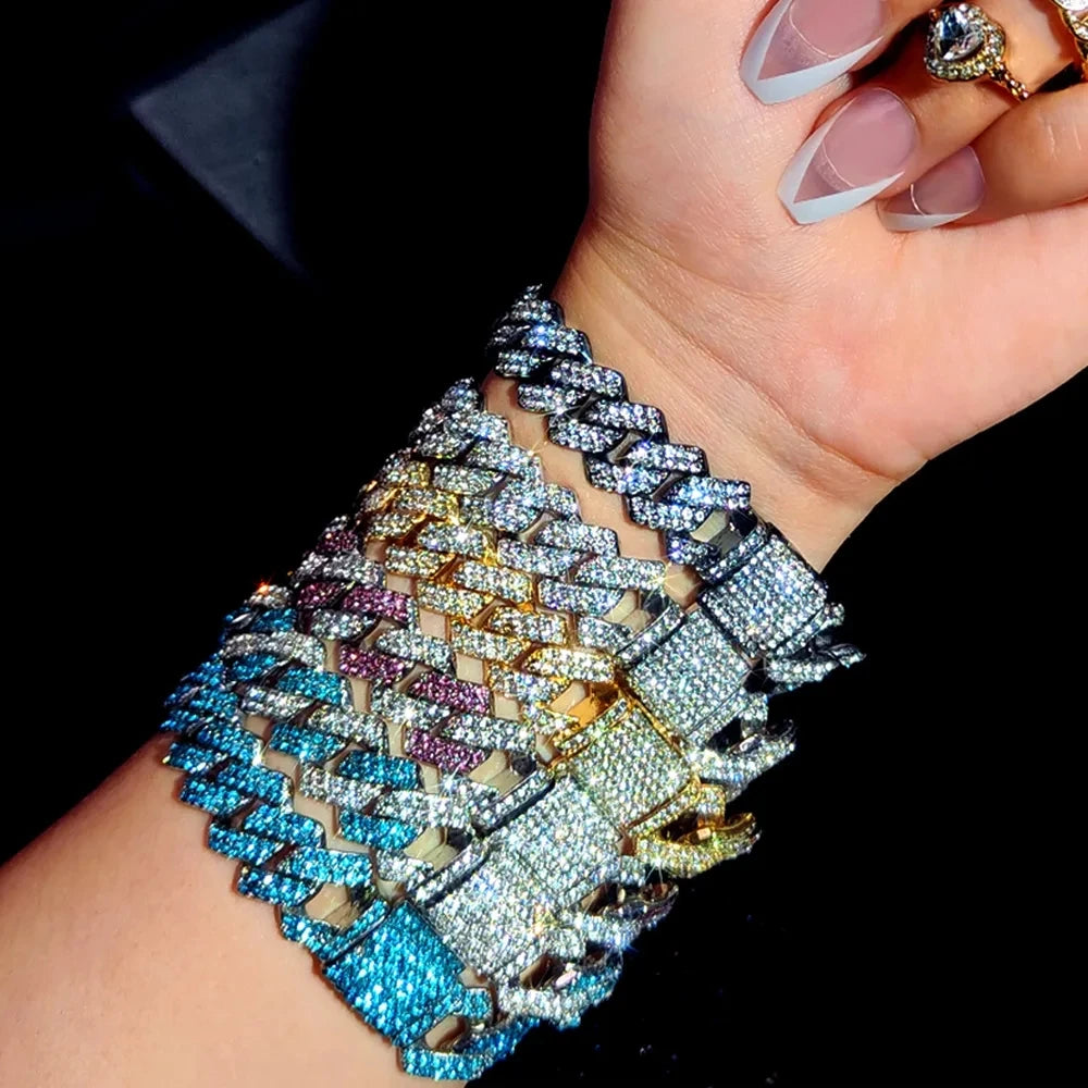 A close-up of a hand wearing an iced-out Cuban link bracelet featuring multicolored rhinestones and pavé stones.