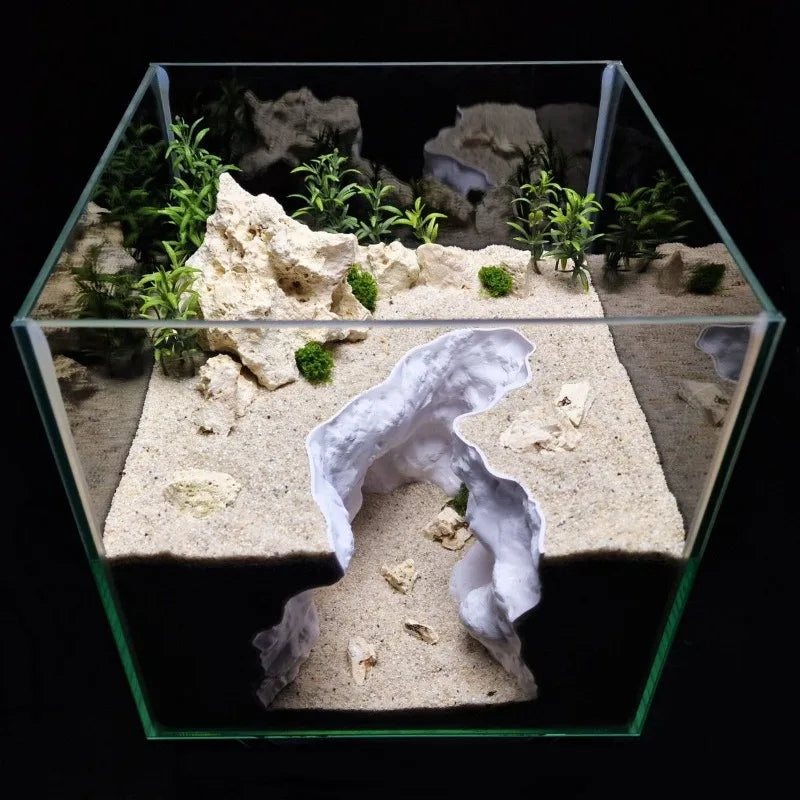 A clear glass aquarium features a miniature natural terrain landscape with rocks and green plants.