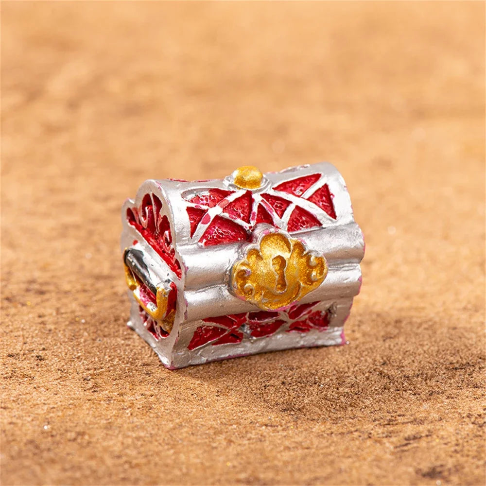 A miniature resin treasure chest ornament with silver and red detailing sits on a brown textured surface.