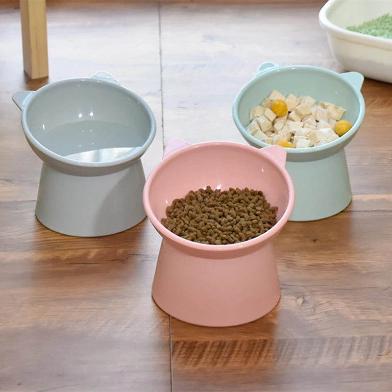 Three ceramic pet bowls of varying sizes and colors sit on a wooden floor.