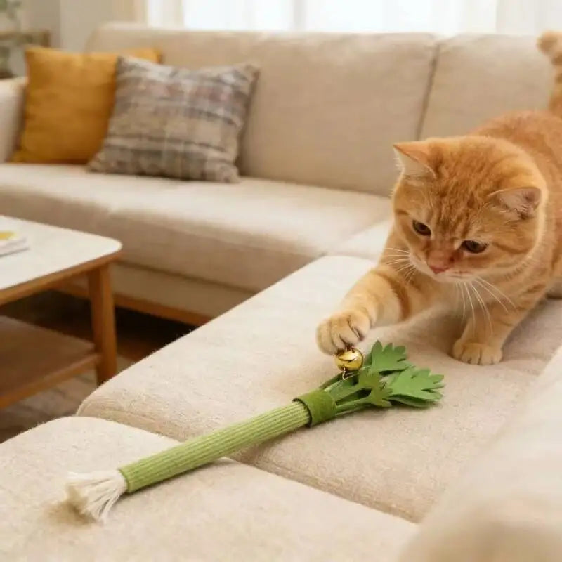 An orange tabby cat playing with a green celery chew toy that has a bell attached.