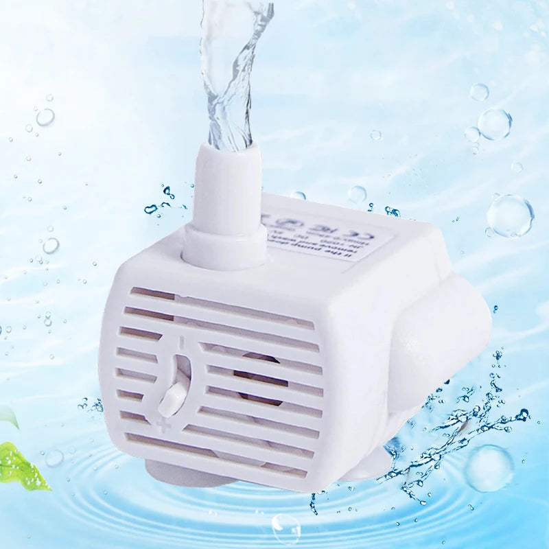 A white pet fountain water pump device is shown with water flowing, surrounded by splashing water droplets.