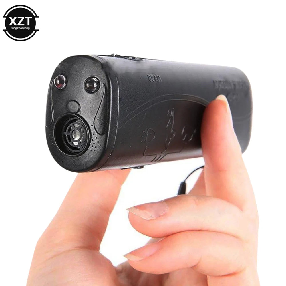 A hand is holding a black ultrasonic dog training device with an LED light feature.