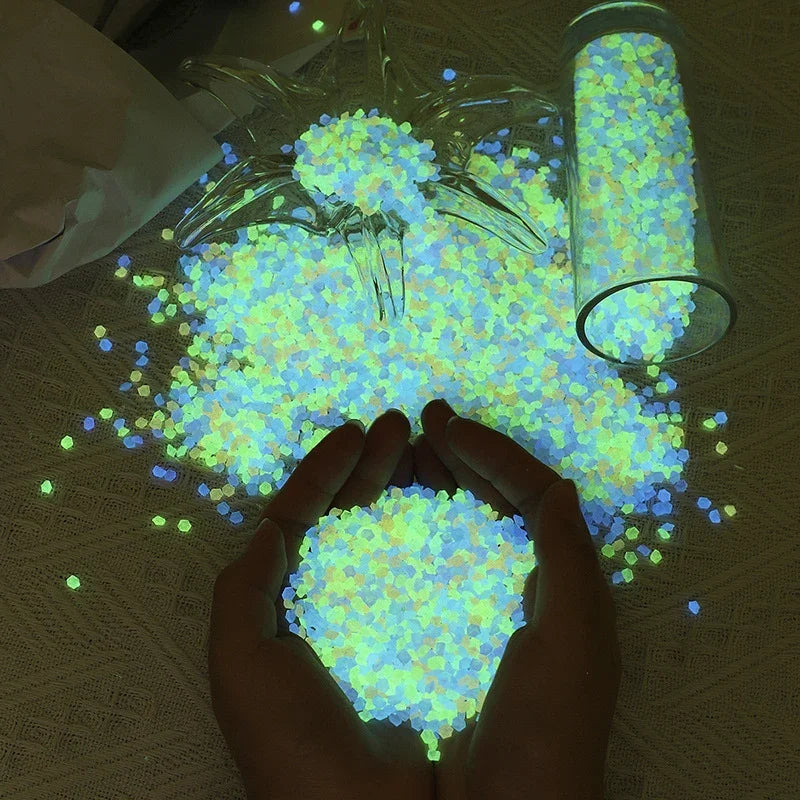 A hand holds a pile of glow-in-the-dark decorative pebbles that emit a bright blue-green light.