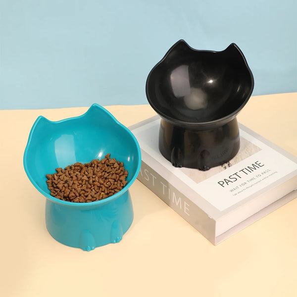 A black elevated cat feeding bowl is shown next to a light blue bowl filled with dry cat food on a white book.